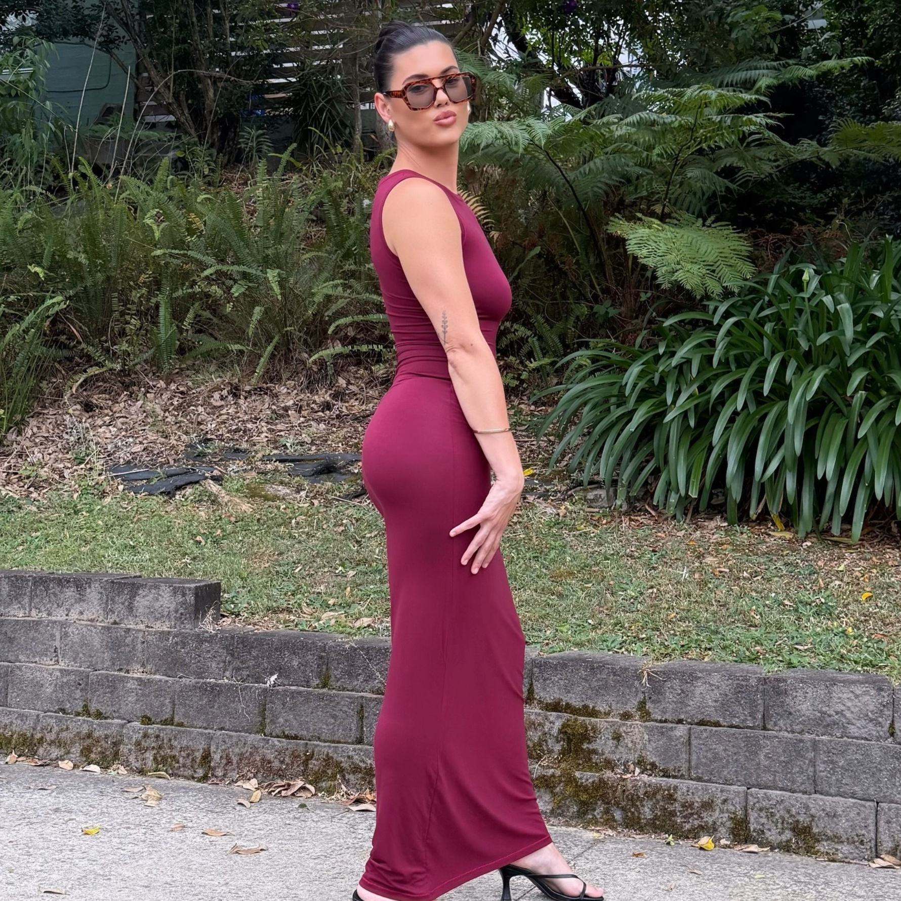Woman in a burgundy dress standing outdoors with greenery in the background