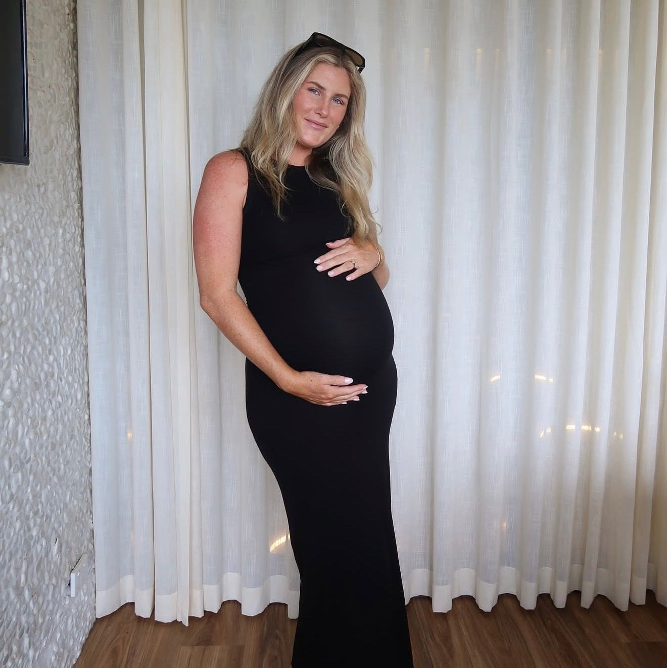 Pregnant woman in a black dress standing in front of white curtains.