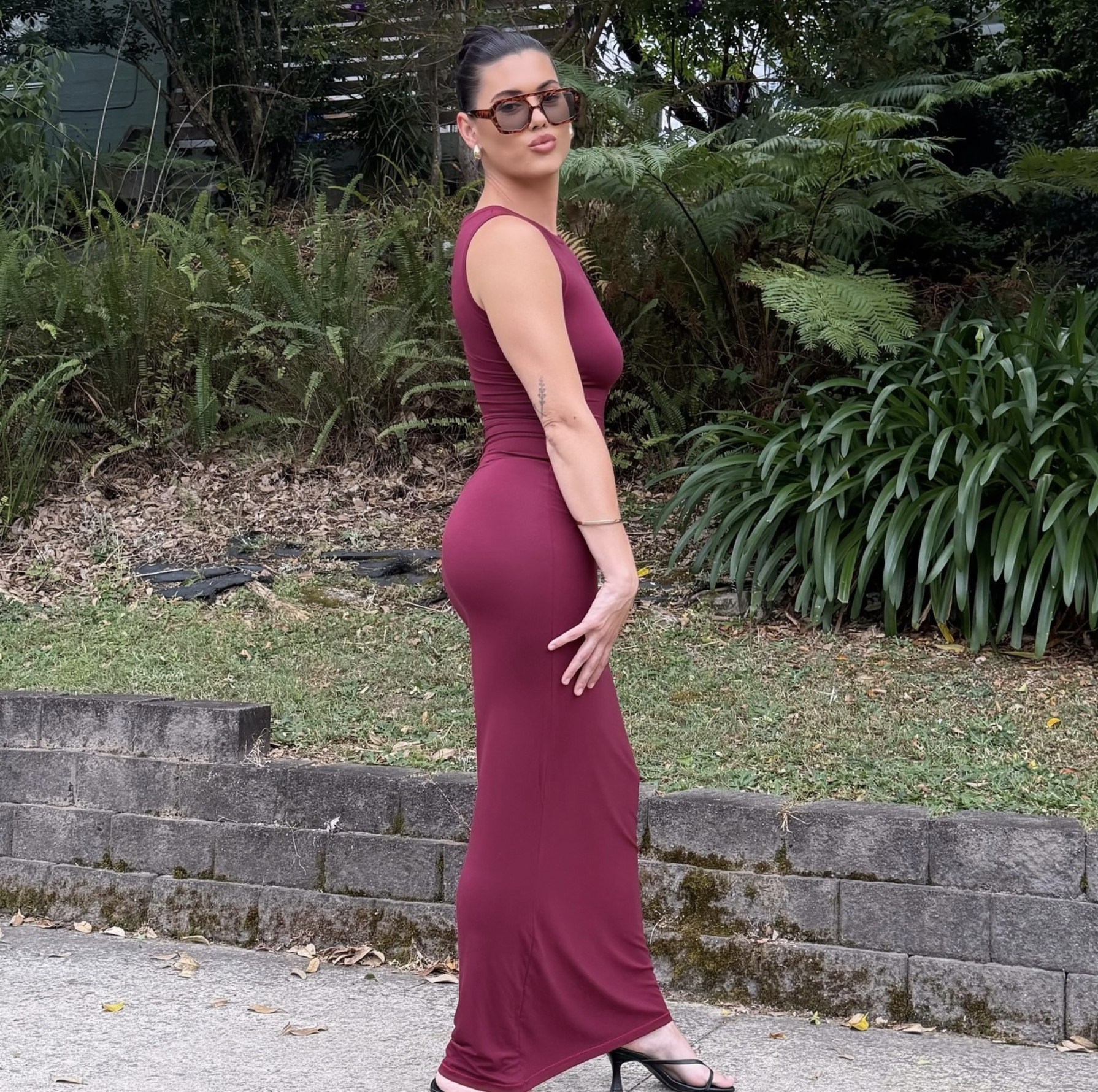 Woman in a burgundy dress standing outdoors with greenery in the background