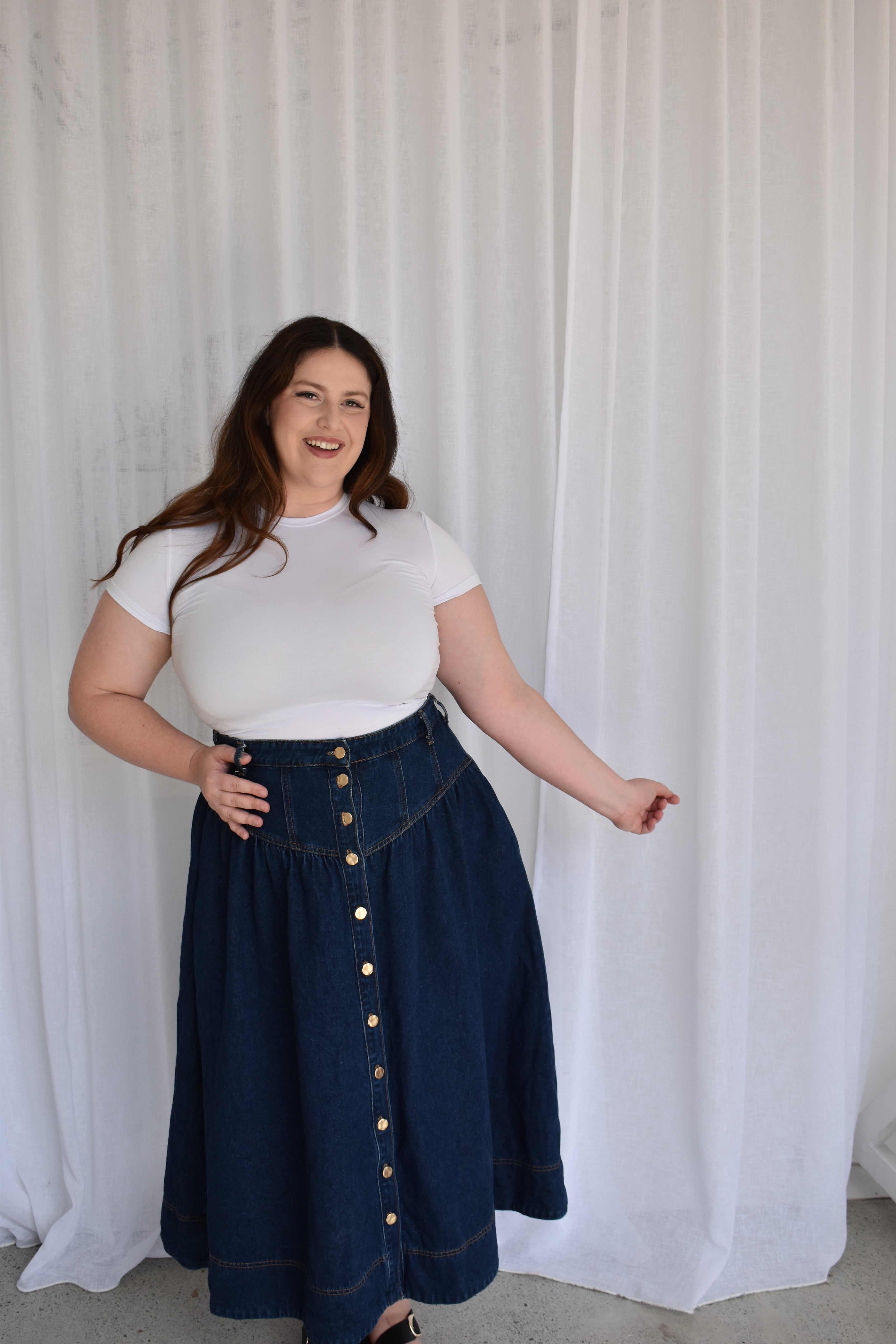 Woman wearing a white top and blue skirt with gold buttons on a white background